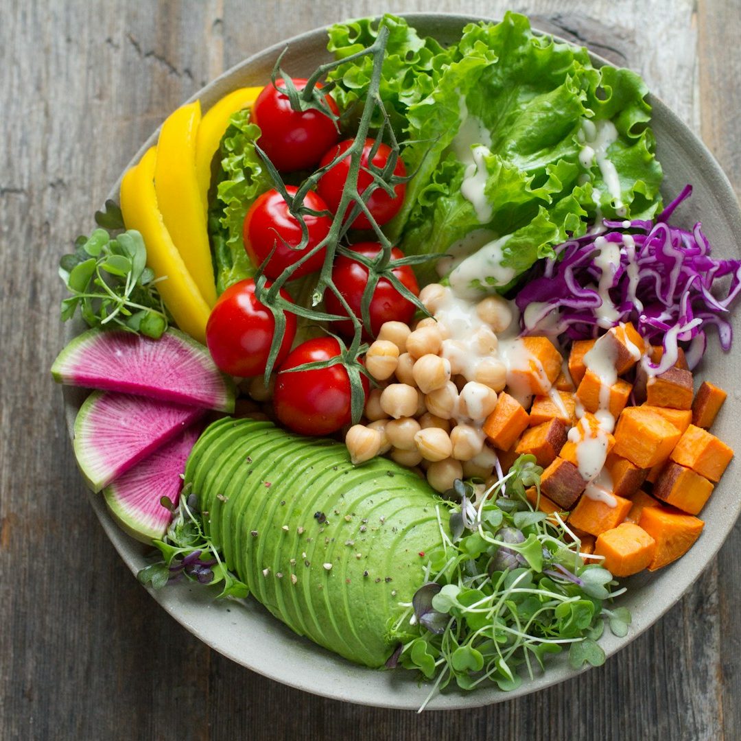 A colorful salad with greens, tomatoes, avocado, sweet potato, and various vegetables.