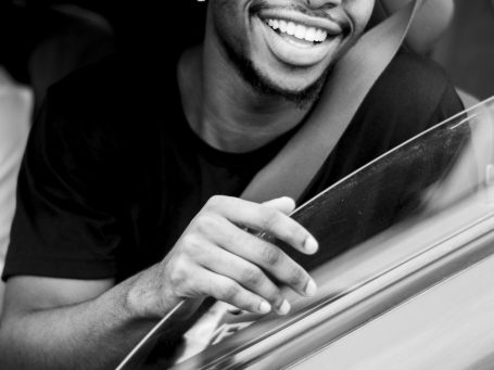 Smiling man leaning out of a car window, wearing a black shirt.
