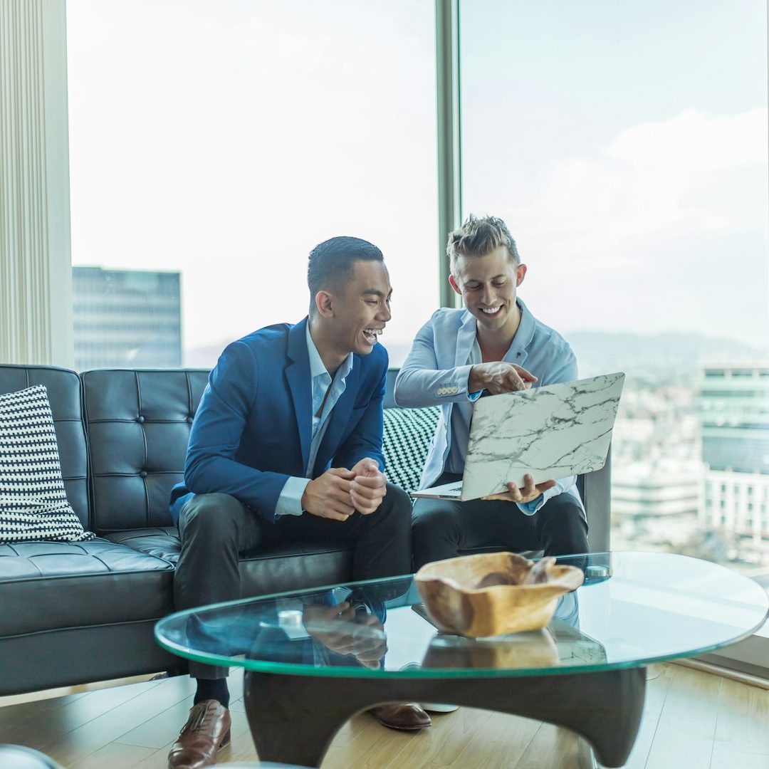 Two men in a modern office discussing a document while sitting on a couch.