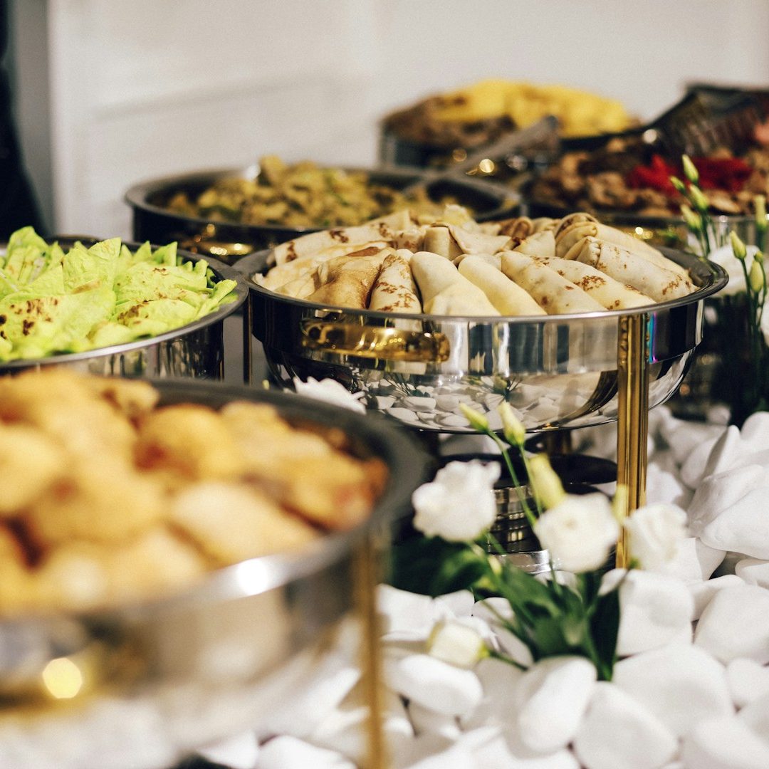 Various colorful food dishes in silver bowls, surrounded by decorative flowers.