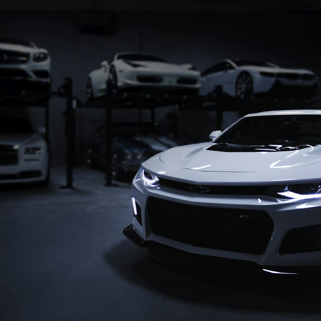 A sleek white sports car parked in a dimly lit garage with other cars on lifts.